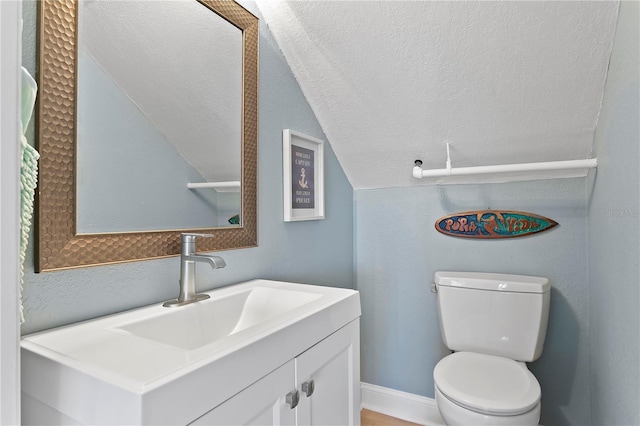 half bath with toilet, a textured ceiling, baseboards, vanity, and vaulted ceiling