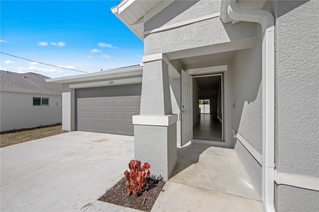 entrance to property featuring stucco siding, a garage, and driveway