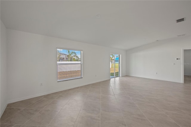 empty room featuring light tile patterned flooring, visible vents, baseboards, and vaulted ceiling