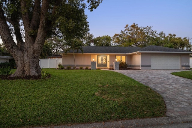 ranch-style home featuring a front yard, fence, driveway, an attached garage, and stucco siding