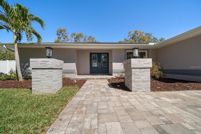 entrance to property with stucco siding, french doors, and fence