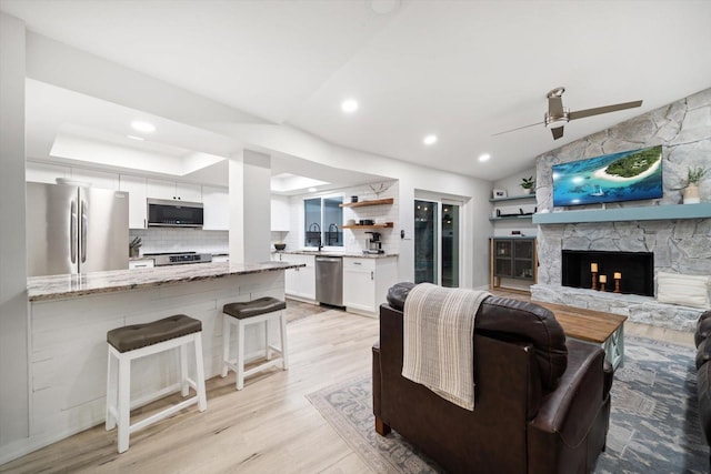 living area featuring ceiling fan, light wood-type flooring, vaulted ceiling, a stone fireplace, and recessed lighting