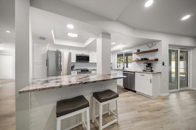 kitchen with a tray ceiling, a kitchen breakfast bar, light wood-style floors, white cabinets, and stainless steel appliances