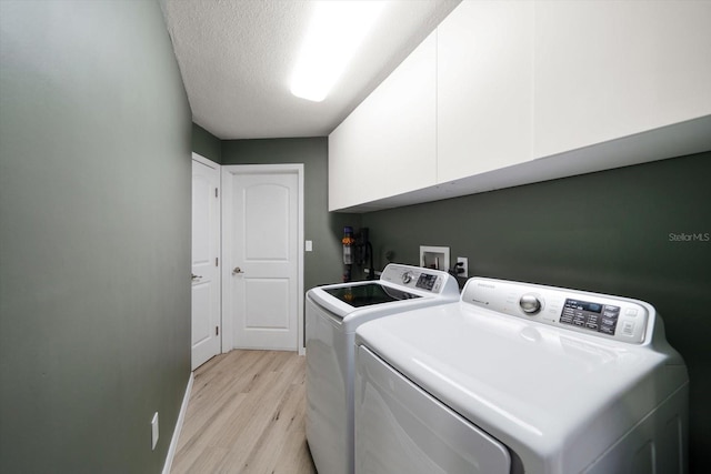 washroom with light wood-type flooring, cabinet space, a textured ceiling, and washer and clothes dryer