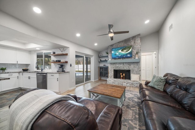 living room featuring lofted ceiling, a stone fireplace, recessed lighting, light wood-style flooring, and a ceiling fan