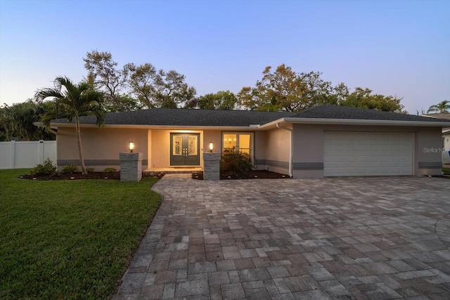 ranch-style house featuring a front yard, stucco siding, french doors, decorative driveway, and an attached garage