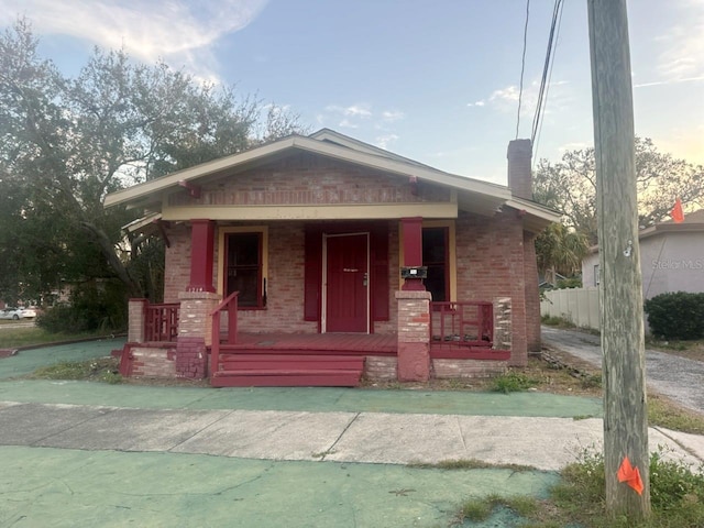 view of front of house featuring a porch, brick siding, and a chimney