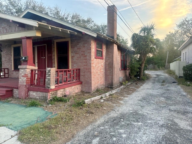 view of side of property with brick siding, covered porch, driveway, and a chimney