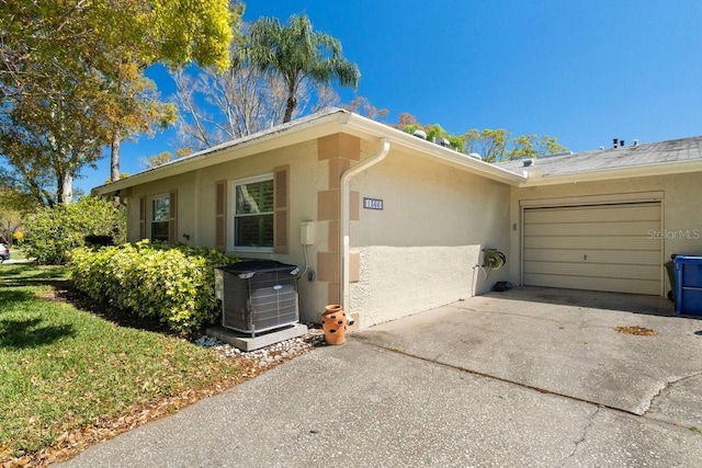 view of side of home featuring stucco siding, a garage, central AC, and driveway