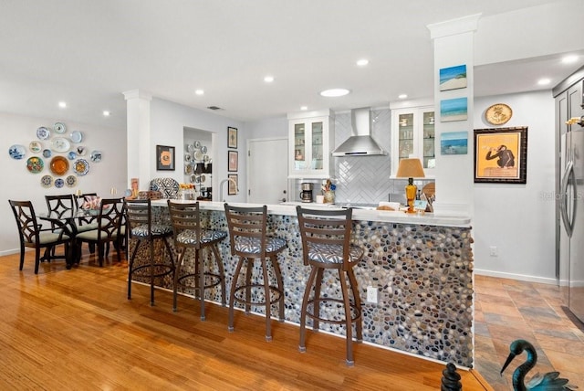 kitchen with baseboards, recessed lighting, light countertops, wall chimney exhaust hood, and backsplash