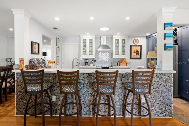 kitchen featuring visible vents, decorative backsplash, light countertops, light wood-style floors, and wall chimney range hood