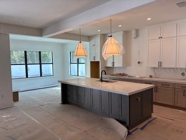 kitchen with white cabinets, visible vents, a kitchen island with sink, and a sink