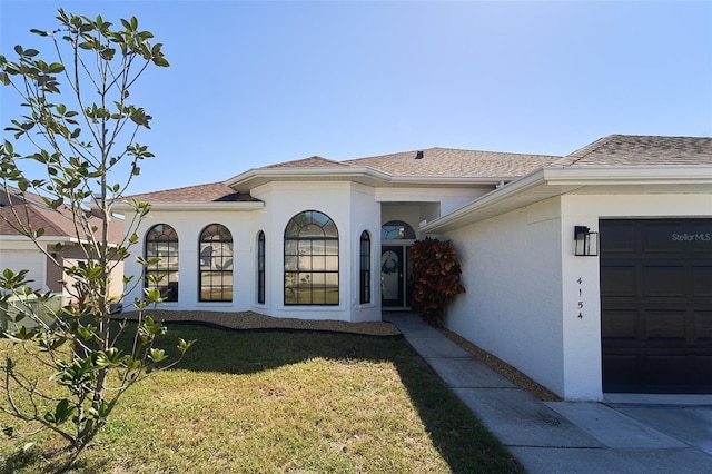 mediterranean / spanish-style house with stucco siding, an attached garage, a shingled roof, and a front yard