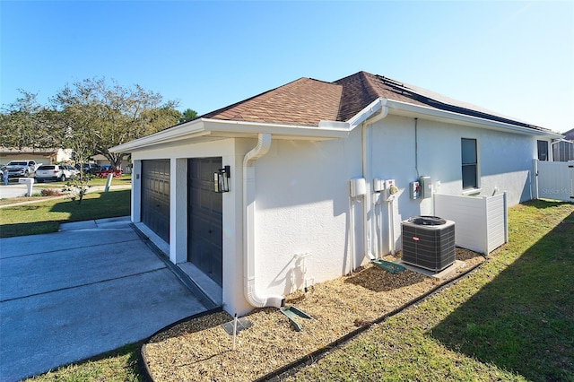 view of side of property with central air condition unit, concrete driveway, roof with shingles, stucco siding, and a lawn