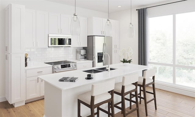 kitchen featuring light wood-type flooring, a kitchen island with sink, a sink, tasteful backsplash, and stainless steel appliances