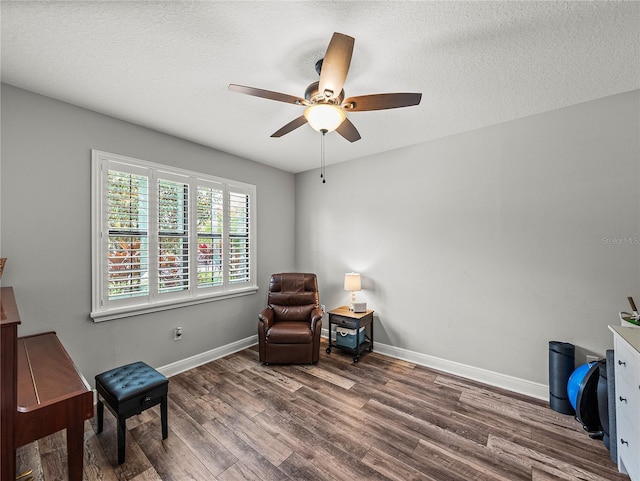 living area featuring a textured ceiling, wood finished floors, baseboards, and ceiling fan