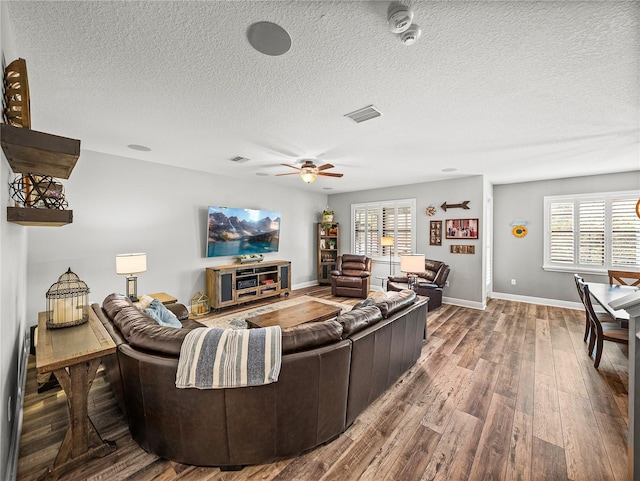 living area with visible vents, baseboards, ceiling fan, wood finished floors, and a textured ceiling