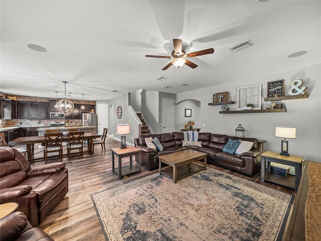 living room featuring visible vents, stairs, light wood-style floors, arched walkways, and a ceiling fan