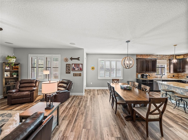 dining space with a textured ceiling, wood finished floors, baseboards, and a chandelier