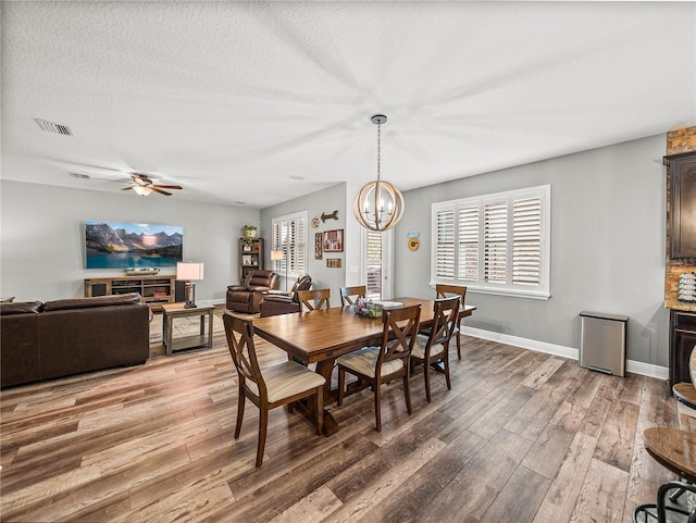 dining room with light wood-type flooring, visible vents, ceiling fan with notable chandelier, a textured ceiling, and baseboards