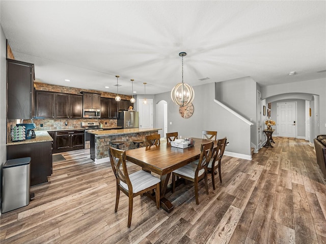 dining area featuring a notable chandelier, wood finished floors, arched walkways, and baseboards