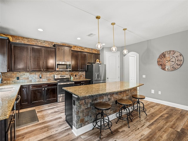 kitchen featuring visible vents, a breakfast bar area, decorative backsplash, arched walkways, and stainless steel appliances