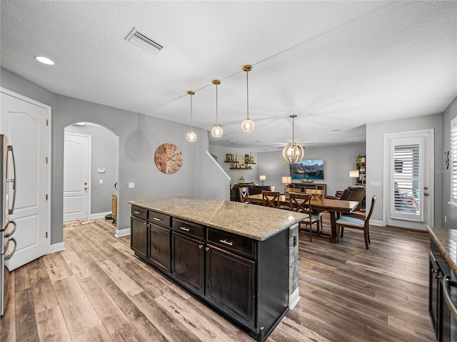 kitchen featuring visible vents, decorative light fixtures, a kitchen island, arched walkways, and light wood-style floors