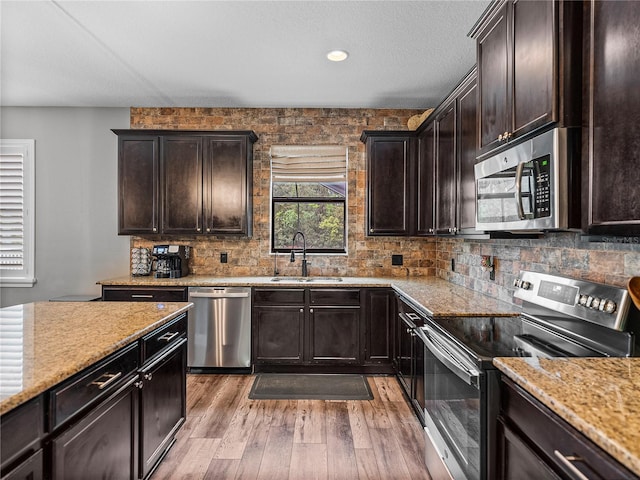 kitchen featuring a sink, decorative backsplash, dark brown cabinets, appliances with stainless steel finishes, and light wood-type flooring