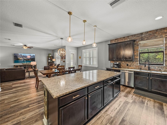 kitchen featuring visible vents, open floor plan, stainless steel dishwasher, wood finished floors, and a sink