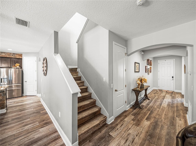 entrance foyer with stairs, dark wood-type flooring, visible vents, and arched walkways