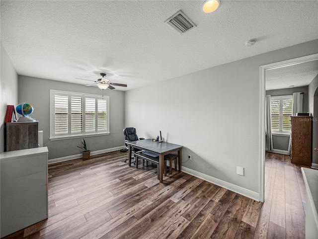 home office with a ceiling fan, wood finished floors, visible vents, baseboards, and a textured ceiling