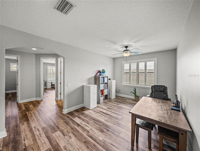 unfurnished office with visible vents, baseboards, ceiling fan, wood finished floors, and arched walkways