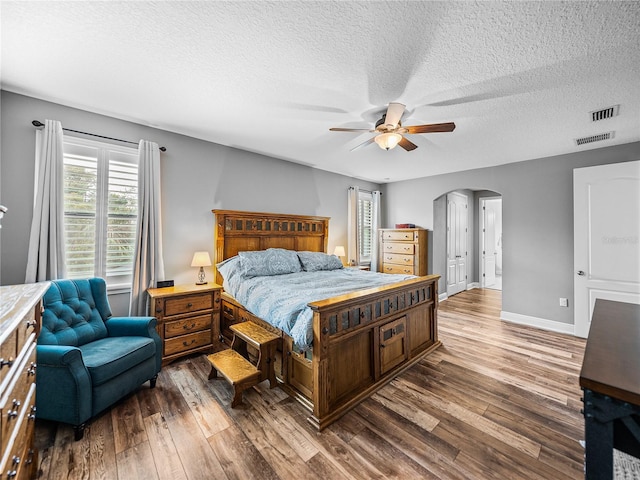 bedroom with hardwood / wood-style floors, baseboards, arched walkways, and ceiling fan