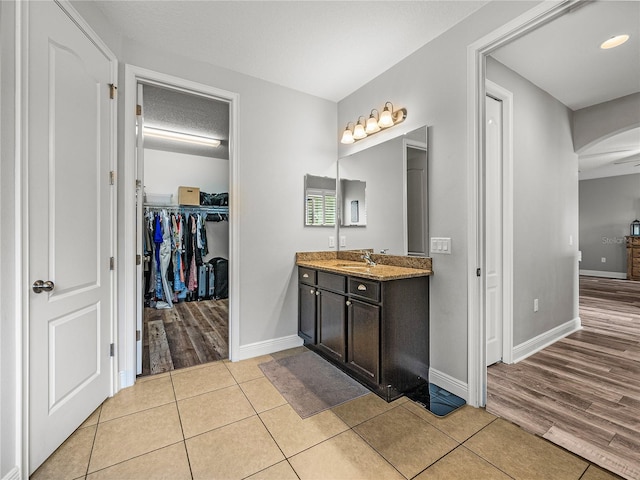 bathroom featuring tile patterned floors, vanity, a walk in closet, and baseboards