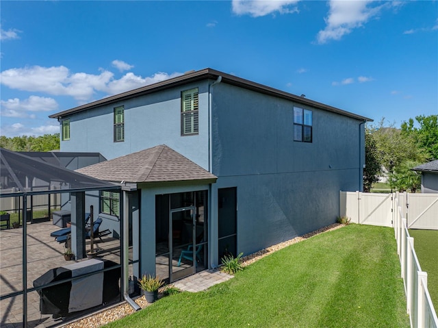 back of property with stucco siding, glass enclosure, a lawn, a patio area, and a gate