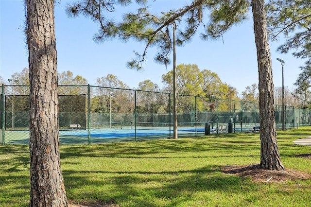 view of tennis court with a yard and fence