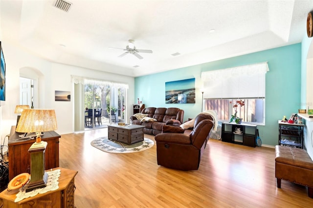 living room featuring visible vents, baseboards, ceiling fan, light wood-type flooring, and arched walkways