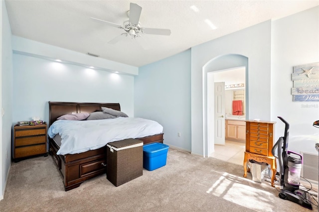 bedroom with visible vents, ceiling fan, light carpet, ensuite bathroom, and arched walkways