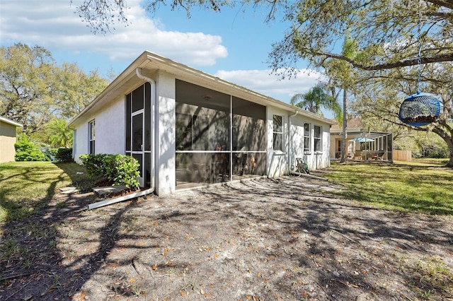 rear view of property with stucco siding, a lawn, and a sunroom