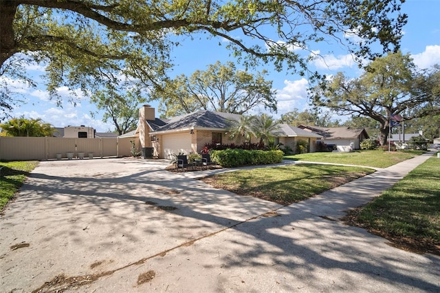 view of side of home with fence, concrete driveway, a chimney, a garage, and a yard