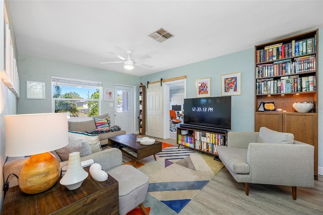 living area featuring a ceiling fan, a barn door, wood finished floors, and visible vents