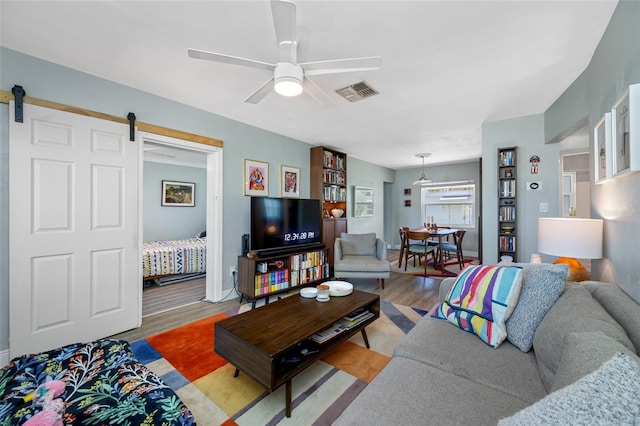 living area featuring light wood finished floors, visible vents, baseboards, a barn door, and a ceiling fan