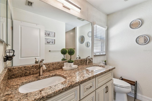 bathroom featuring double vanity, visible vents, toilet, and a sink