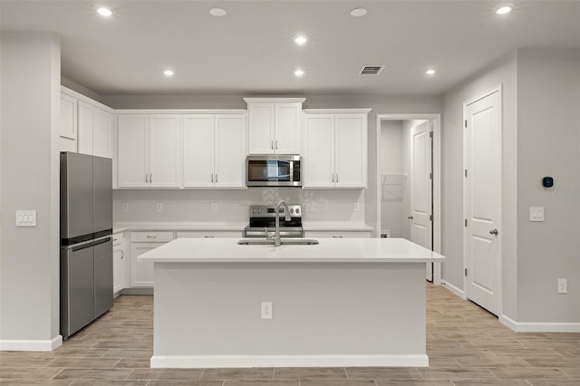20405 Symphony Pl, Venice, FL 34293 - kitchen featuring wood finish floors, visible vents, appliances with stainless steel finishes, a kitchen island with sink, and light countertops