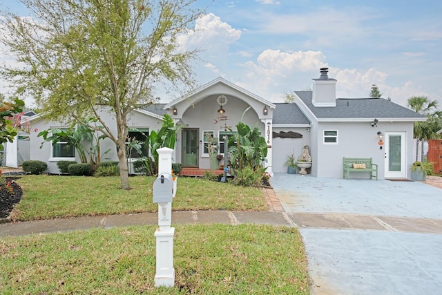 view of front of home featuring stucco siding, a chimney, a front yard, and roof with shingles