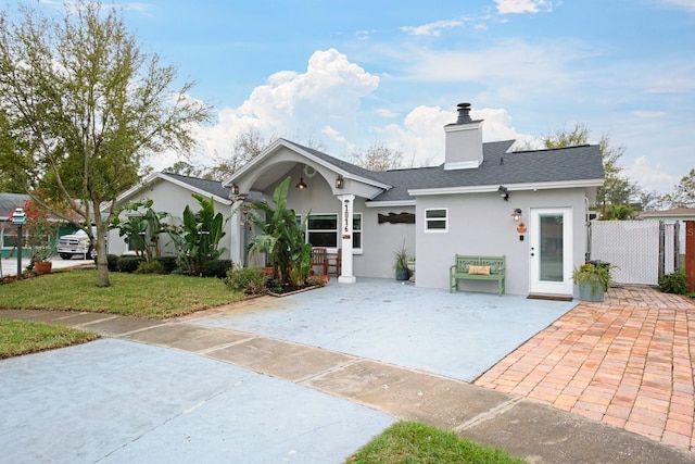 view of front of house featuring stucco siding, a front lawn, a gate, roof with shingles, and a chimney