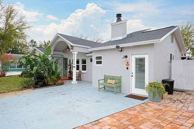 rear view of property featuring stucco siding, a patio, a chimney, and a shingled roof