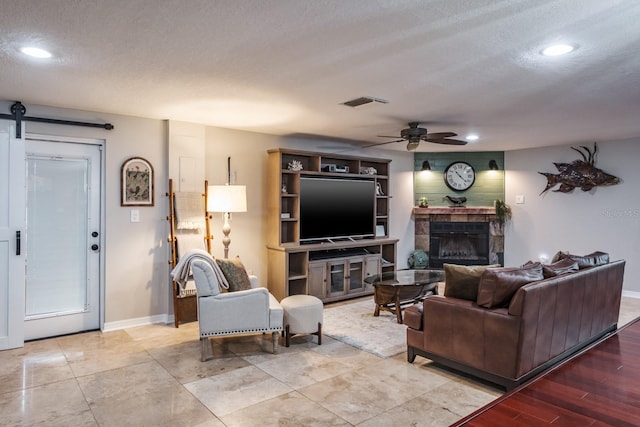 living area with visible vents, a barn door, a tile fireplace, a textured ceiling, and a ceiling fan