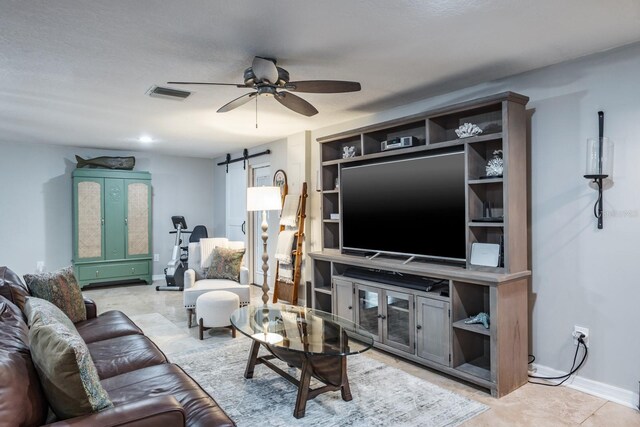 living area featuring a barn door, baseboards, visible vents, and a ceiling fan