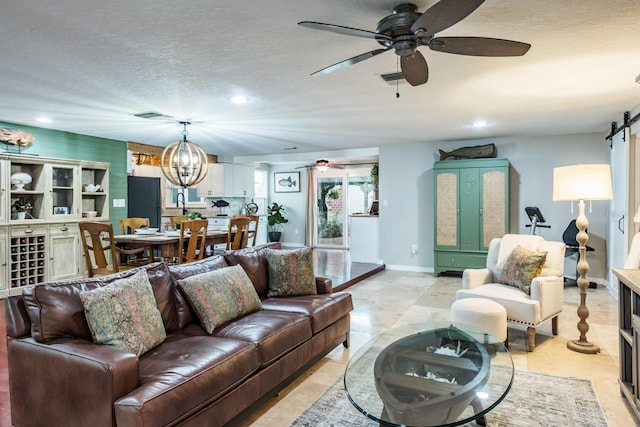 living area with visible vents, ceiling fan with notable chandelier, a textured ceiling, a barn door, and baseboards